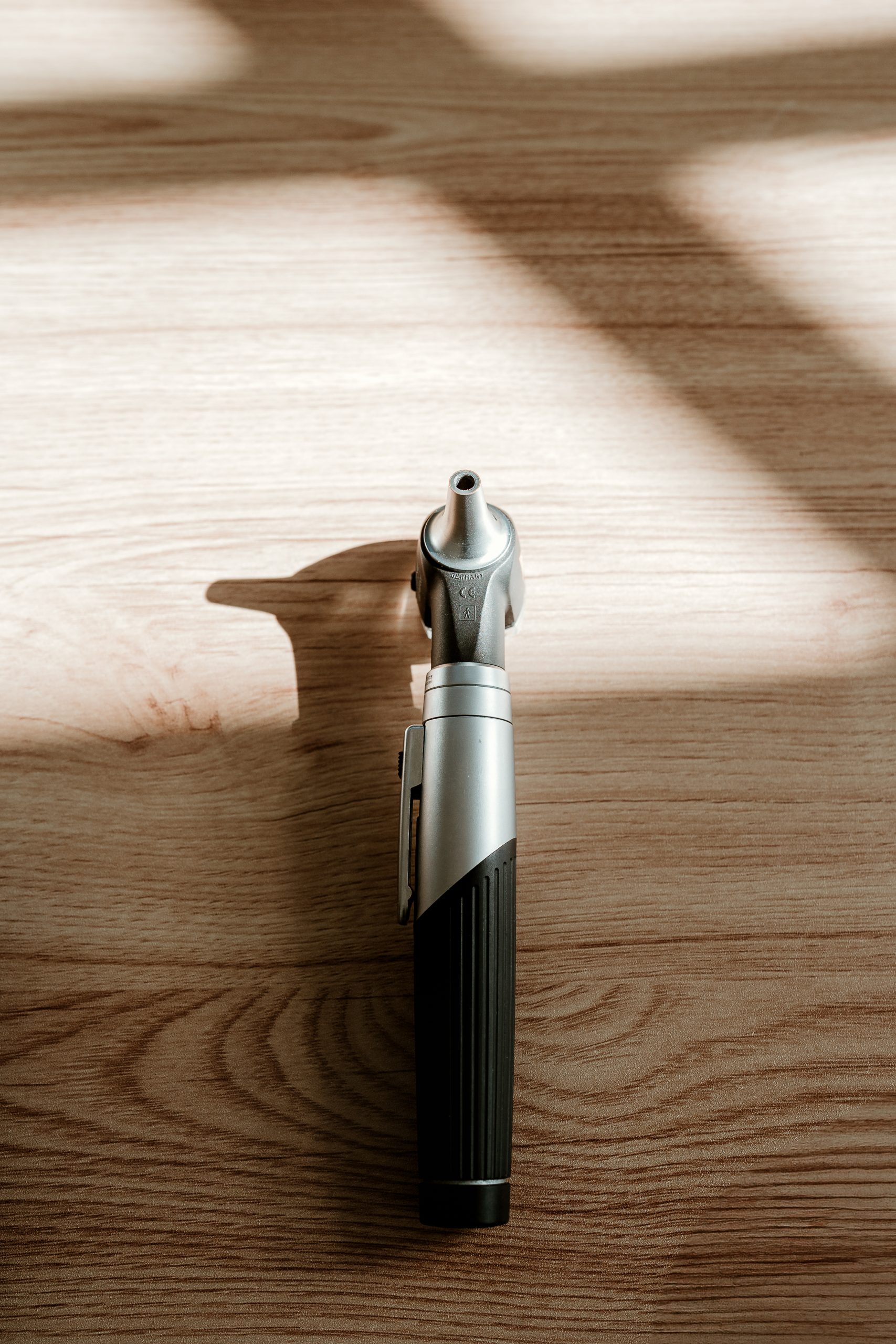 A silver and black otoscope stands on a wooden surface, casting a long shadow, beside information about balance assessments for dizziness.