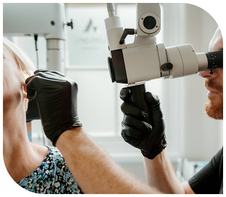 A clinician in black gloves examines a patient's ear through a microscope during a hearing assessment at a Scottish clinic.
