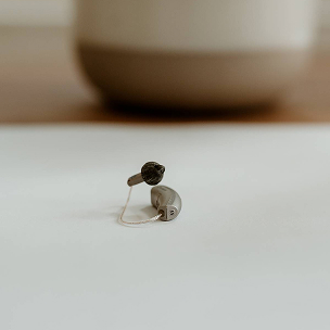 A small beige hearing aid with a fine clear tube rests on a white surface, reflecting Almond Hearing’s Livingston clinic care.
