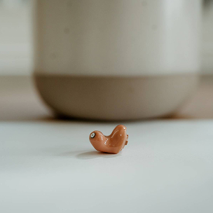 A discreet brown in-ear hearing aid rests on a pale surface before a softly blurred pot, reflecting Almond Hearing’s Livingston clinic.