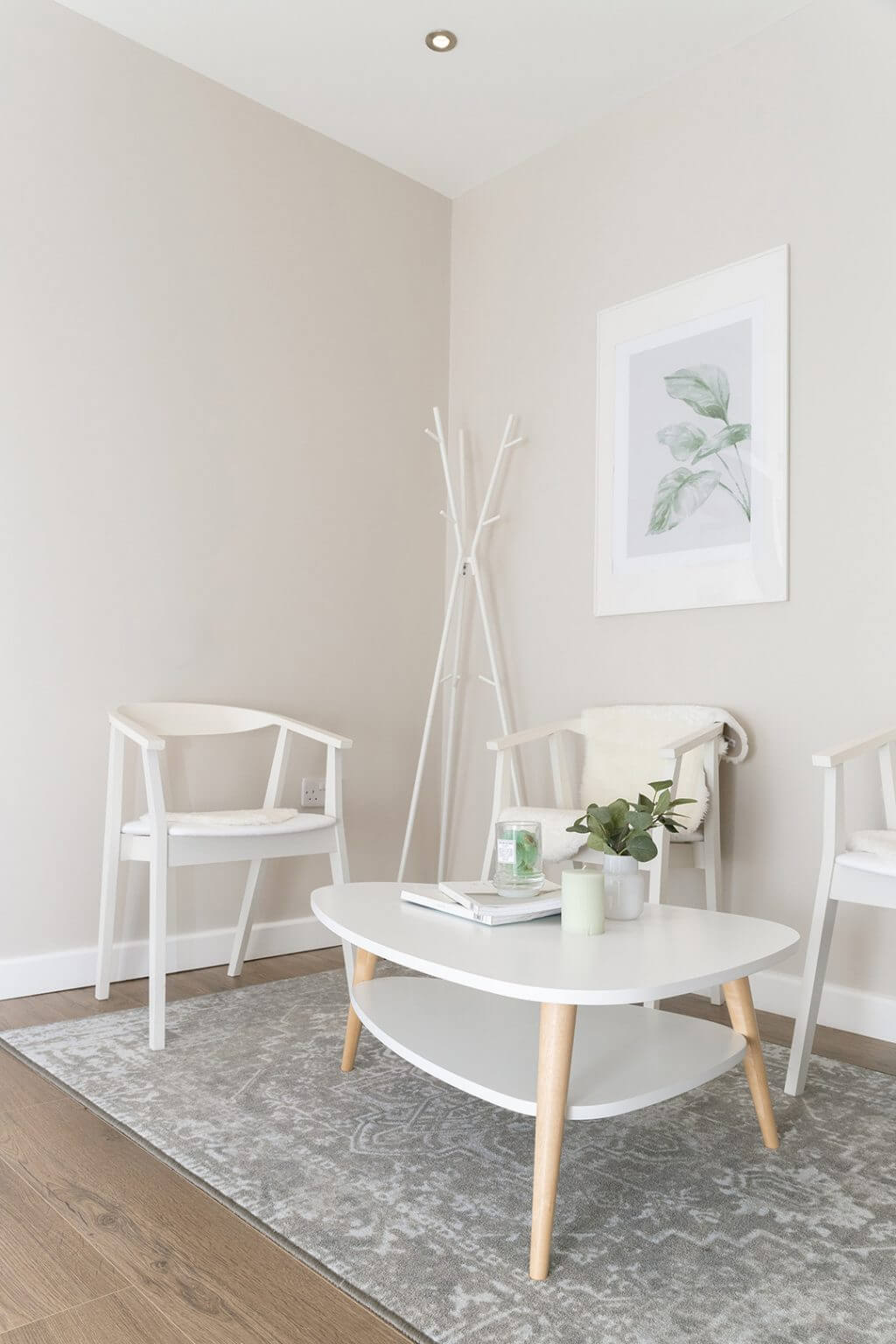 A calm, neutral-toned clinic waiting area in Scotland has white chairs, an oval table, leafy plant and framed botanical print.